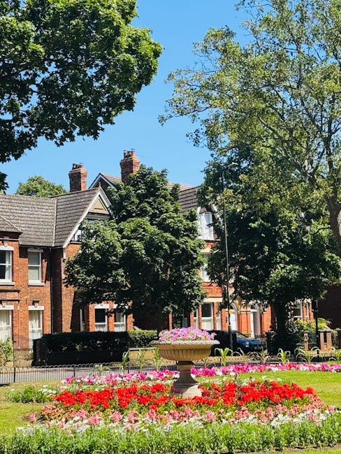 A landscaped garden area on the Grahame Park estate featuring a well-maintained lawn bordered by vibrant flower beds with pink, red, and white blooms. In the middle of the garden, there is a large orn